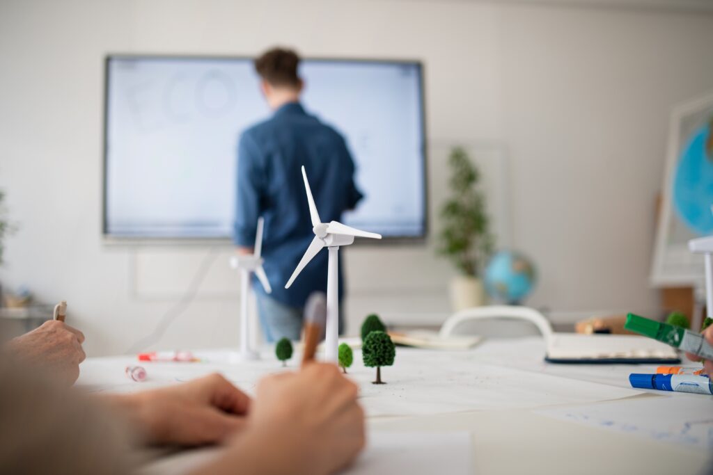Group of senior students discussing altenrative energy with teacher in classroom, close-up of model wind turbine.