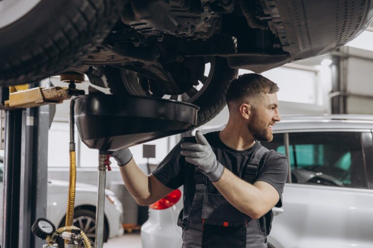 A car workshop worker is draining oil from engine while standing under the car