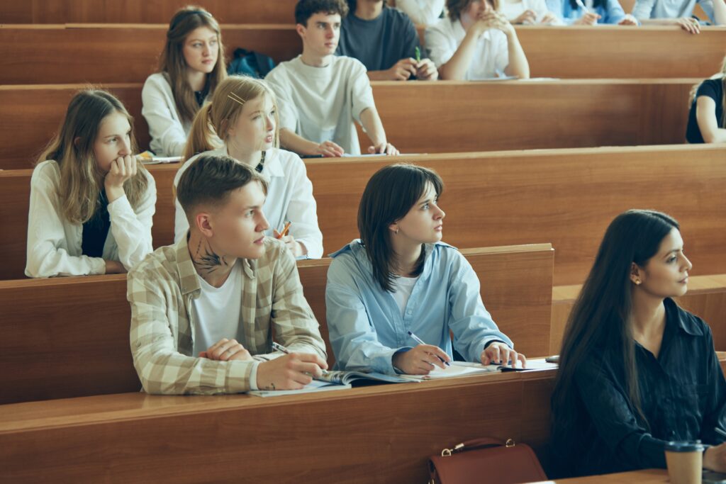 Group of multiethnic people, students sitting in well-lit university auditorium, listening to teacher explaining new theme of subject. Concept of education, youth, workshop, knowledge